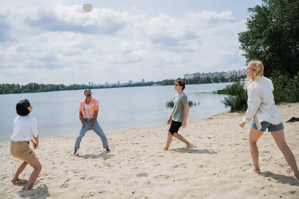 Мультикультурные друзья играют в пляжный волейбол на берегу реки — стоковое фото