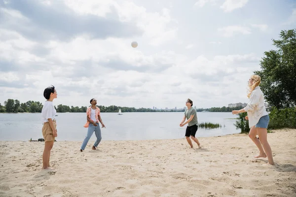 Young multiethnic friends playing volleyball on sand beach near river - foto de stock