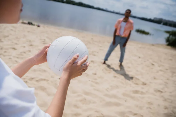 Cropped view of woman holding ball near blurred african american man on riverside — Stockfoto