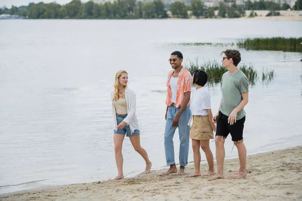 Full length of young and happy multiethnic friends walking on summer beach — Photo de stock