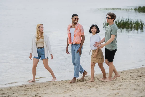Young man talking to interracial friends while walking together on riverside — Stock Photo