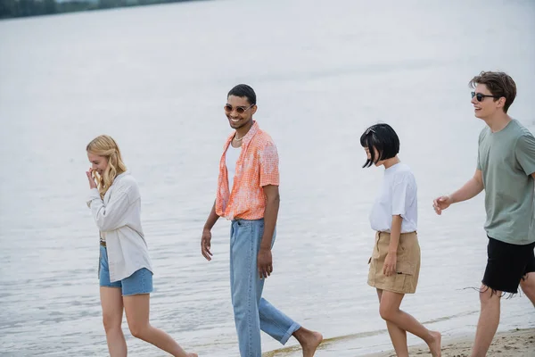 Cheerful interracial friends walking along riverside — Stock Photo