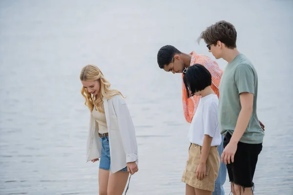 Young interracial friends standing near river on summer day — Fotografia de Stock