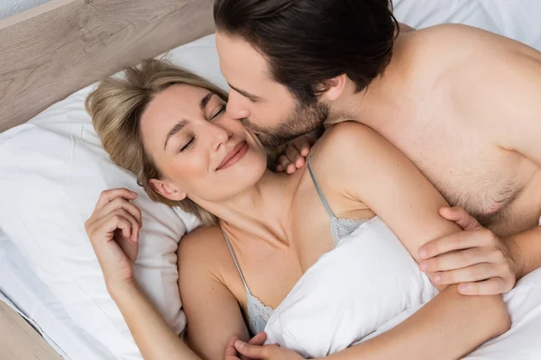 Top view of man kissing smiling blonde woman while waking her in morning - foto de stock