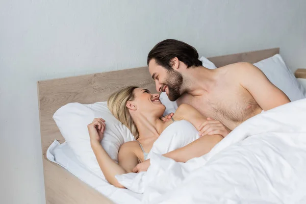 Happy couple smiling at each other on bed in morning - foto de stock