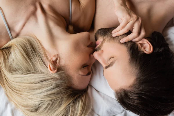 Вид сверху на сексуальную блондинку и небритого брюнета, целующегося с закрытыми глазами в постели — стоковое фото