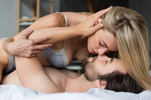 Мужчина с закрытыми глазами трогает волосы блондинки и целуется на кровати — стоковое фото