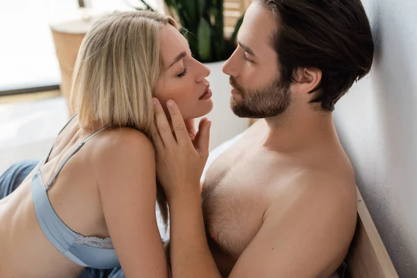 Brunette man touching face of passionate blonde woman in bedroom — Stock Photo