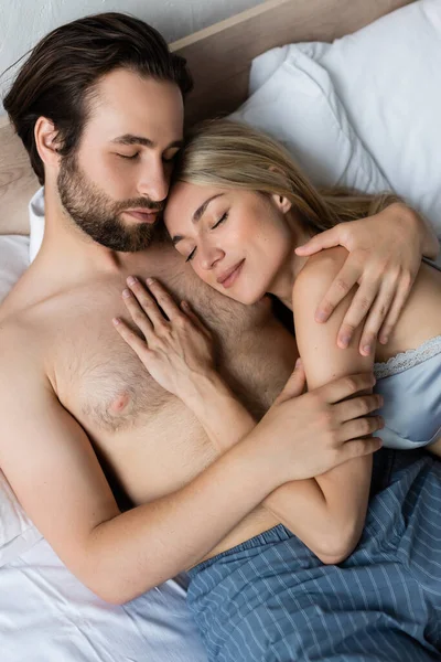 Top view of sexy couple embracing while lying on bed with closed eyes — Fotografia de Stock