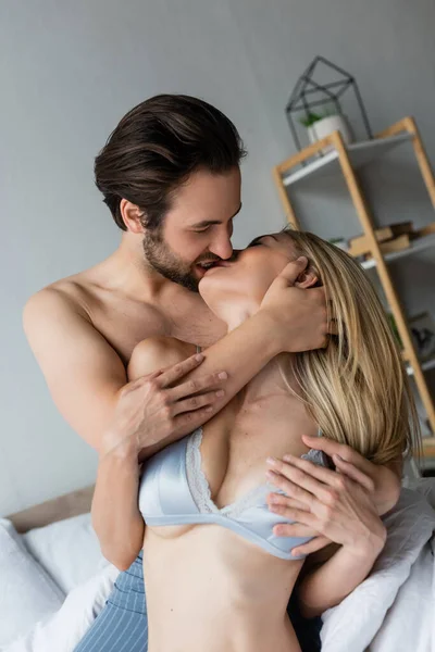 Brunette man hugging seductive woman in sexy underwear and kissing her in bedroom — Stock Photo