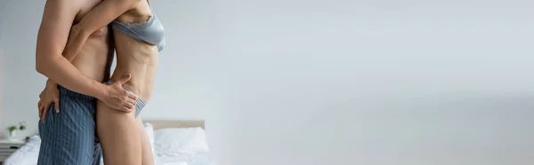 Cropped view of man in pajama pants hugging woman in sexy underwear in bedroom, banner — Stock Photo