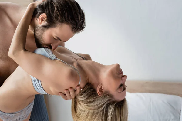 Side view of brunette man kissing breast of passionate blonde woman in underwear — Fotografia de Stock