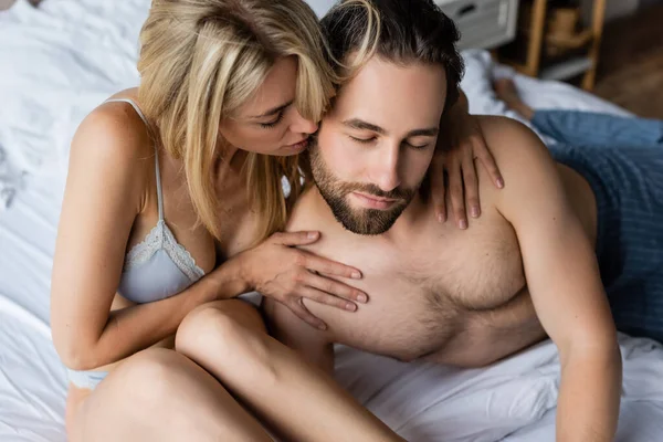 Blonde passionate woman seducing man with closed eyes in bedroom — Stock Photo