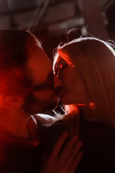 Low angle view of couple in sunglasses kissing during party with lighting — Stock Photo