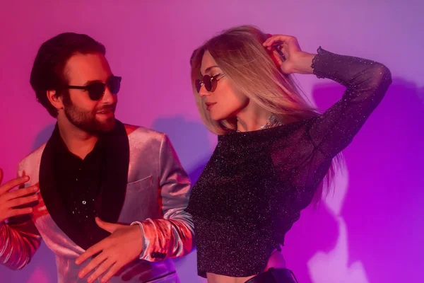 Стильная пара в солнечных очках танцует во время вечеринки на фиолетовом фоне — стоковое фото