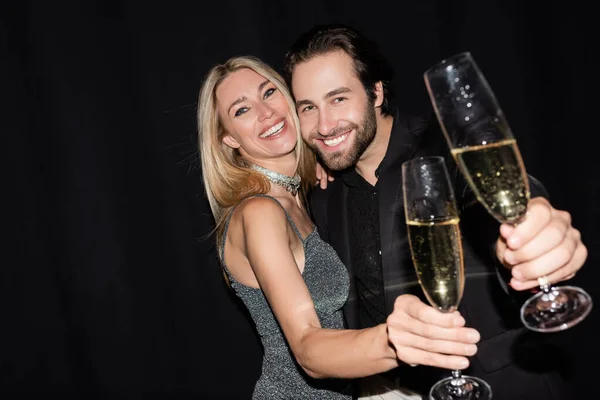 Blonde woman in dress hugging boyfriend and holding glass of champagne isolated on black - foto de stock