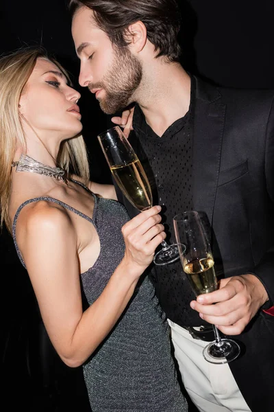 Side view of sexy couple holding glasses of champagne during party isolated on black — Stock Photo