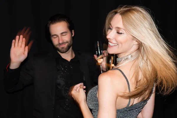 Motion blur of smiling woman with champagne dancing with boyfriend isolated on black — Stock Photo