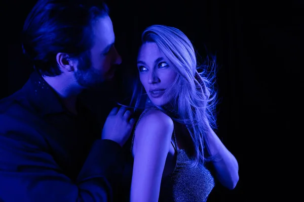 Sexy blonde woman looking at boyfriend with blue lighting isolated on black — Stock Photo