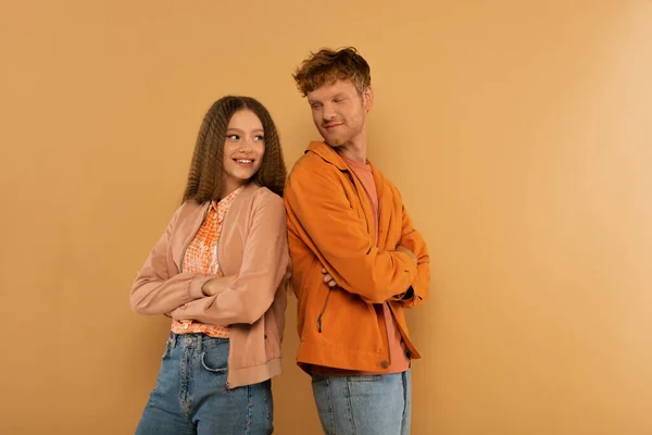 Happy young couple in jackets standing with crossed arms isolated on beige — стоковое фото