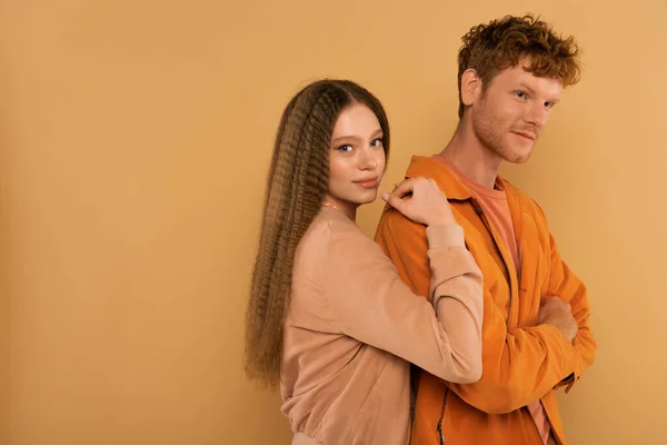 Teenage girl with wavy hair hugging redhead boyfriend isolated on beige — стоковое фото