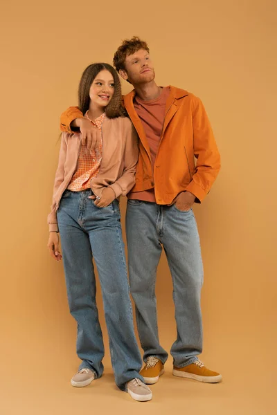 Full length of happy young man in autumnal outfit and gumshoes hugging girlfriend on beige — Photo de stock