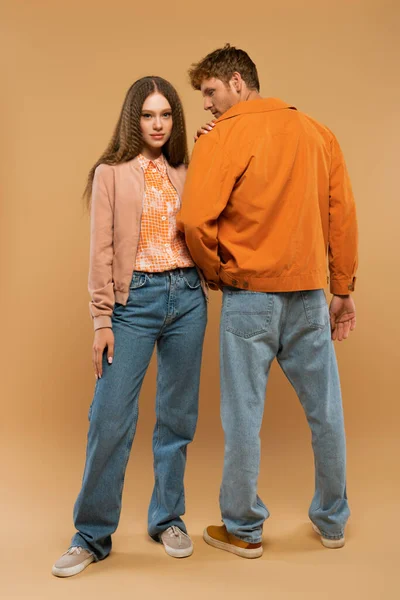 Full length of young couple in autumnal outfits and gumshoes posing on beige - foto de stock