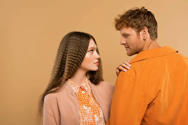 Side view of young couple in jackets looking at each other isolated on beige — Stockfoto