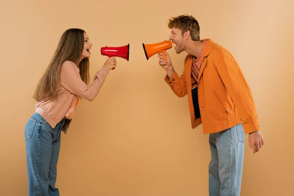 Side view of young couple screaming in loudspeakers and smiling isolated on beige — Stockfoto