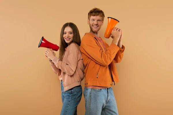 Cheerful young couple holding loudspeakers and standing isolated on beige — Fotografia de Stock