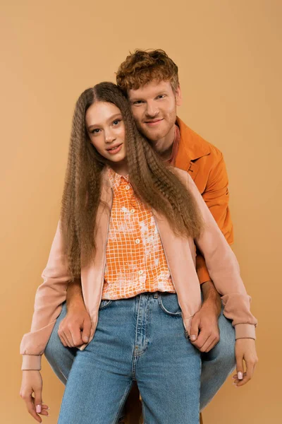 Cheerful young man hugging girlfriend with wavy hair isolated on beige — Fotografia de Stock