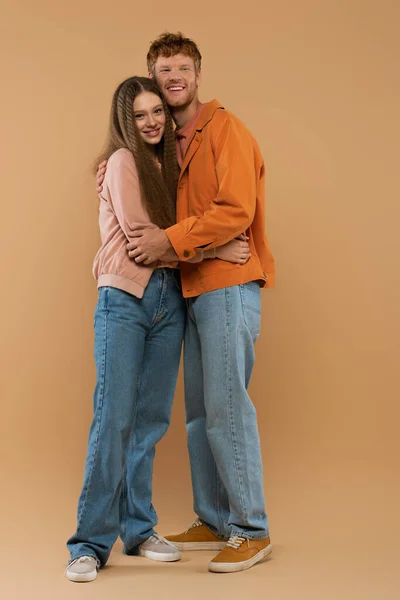 Full length of young and cheerful couple hugging while standing on beige - foto de stock