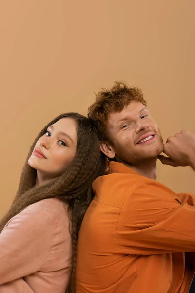 Smiling young man with red hair sitting back to back with pretty girlfriend isolated on beige — Stock Photo
