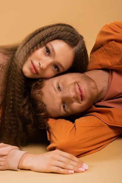 Happy and young redhead man lying together with pretty girlfriend isolated on beige — стоковое фото