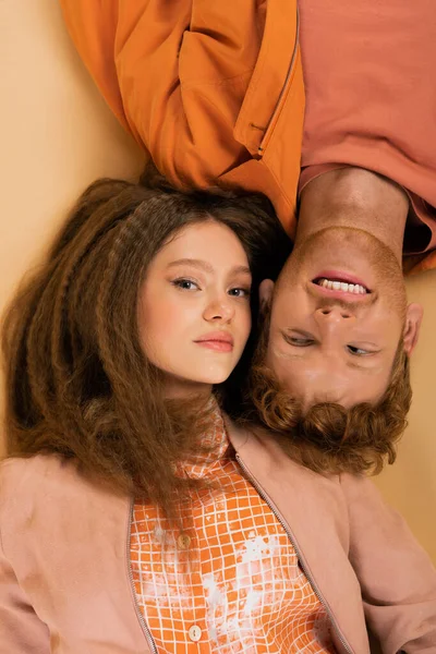 Top view of happy and young redhead man lying together with pretty girlfriend on beige — Stock Photo