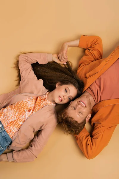 Top view of joyful and young redhead man lying together with pretty girlfriend on beige — Stock Photo