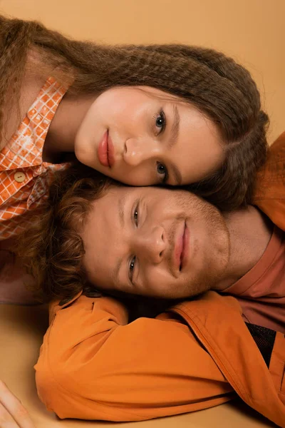 Top view of positive and young redhead man lying together with pretty girlfriend isolated on beige — стоковое фото