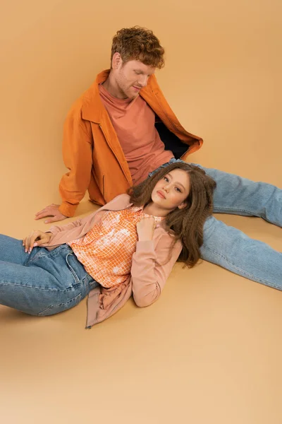 Teenage girl with wavy hair lying on redhead boyfriend in jeans on orange — Photo de stock