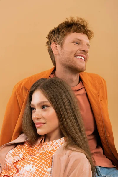 Cheerful redhead man smiling near pretty and happy girl isolated on beige - foto de stock