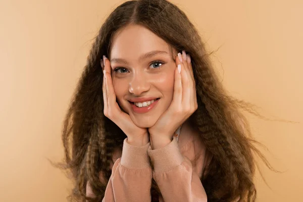 Joyful teenage girl looking at camera while posing with hands near cheeks isolated on beige — Stock Photo