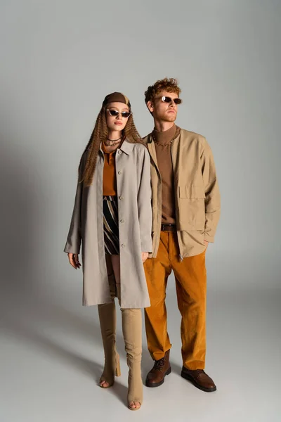 Full length of young and stylish couple in autumnal outfits posing on grey — Photo de stock