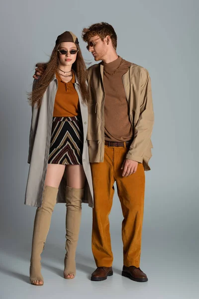 Full length of young stylish couple in autumnal outfits and trendy sunglasses standing on grey — Stockfoto