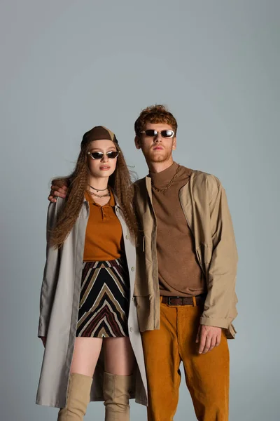 Young couple in autumnal outfits and trendy sunglasses standing isolated on grey — стоковое фото