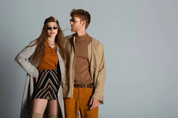 Stylish couple in autumnal outfits and trendy sunglasses standing isolated on grey — Photo de stock