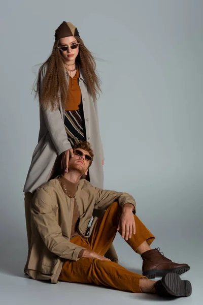 Full length of teenage girl in trench coat standing near stylish boyfriend on grey — Foto stock