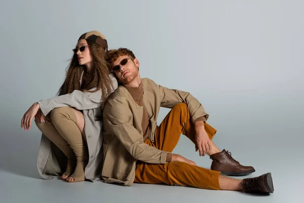 Full length of young and stylish couple in autumnal outfits sitting together on grey — Fotografia de Stock