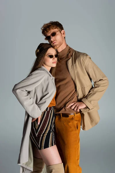 Молода пара в сонцезахисних окулярах і автентичний одяг позує разом ізольовано на сірому — стокове фото