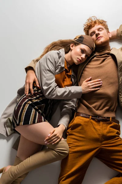 Top view of stylish young man and girl in autumnal outfits lying together on grey — Fotografia de Stock