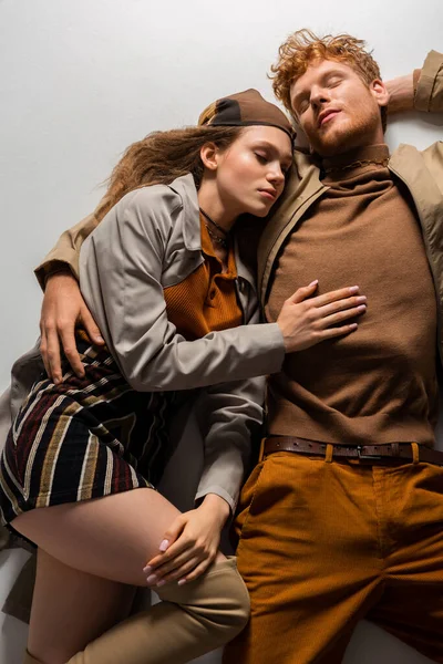 Top view of stylish young couple with closed eyes lying in autumnal outfits on grey — Fotografia de Stock