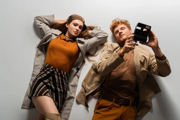 Top view of young man in stylish outfit holding vintage camera and lying together with girlfriend on grey — Stock Photo